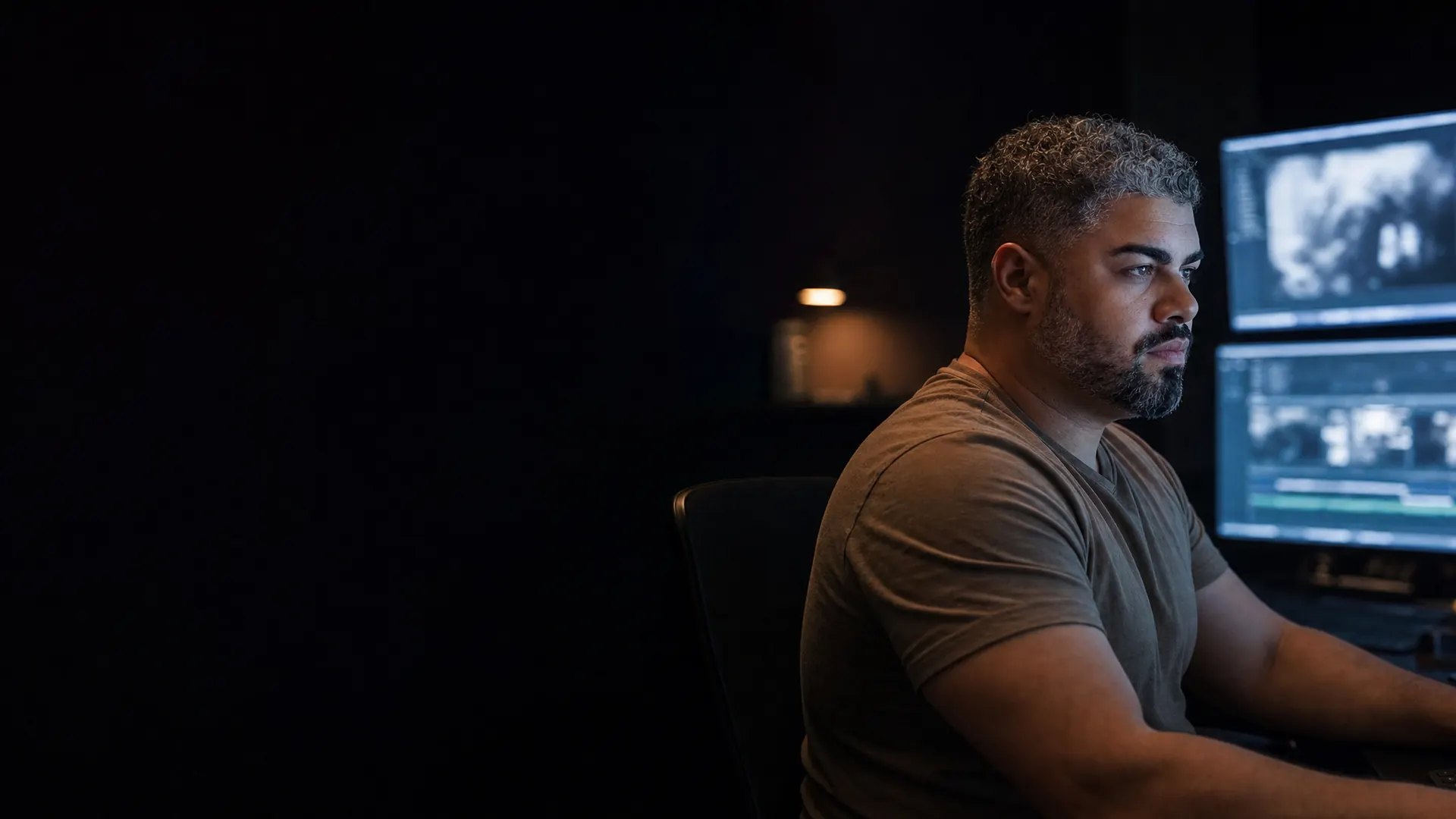 Erick Antunes de perfil numa sala de edição escura, iluminado pelos monitores com frames de um filme.
